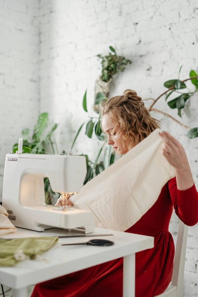 Woman in Red Long Sleeve Dress Sitting on Chair Sewing