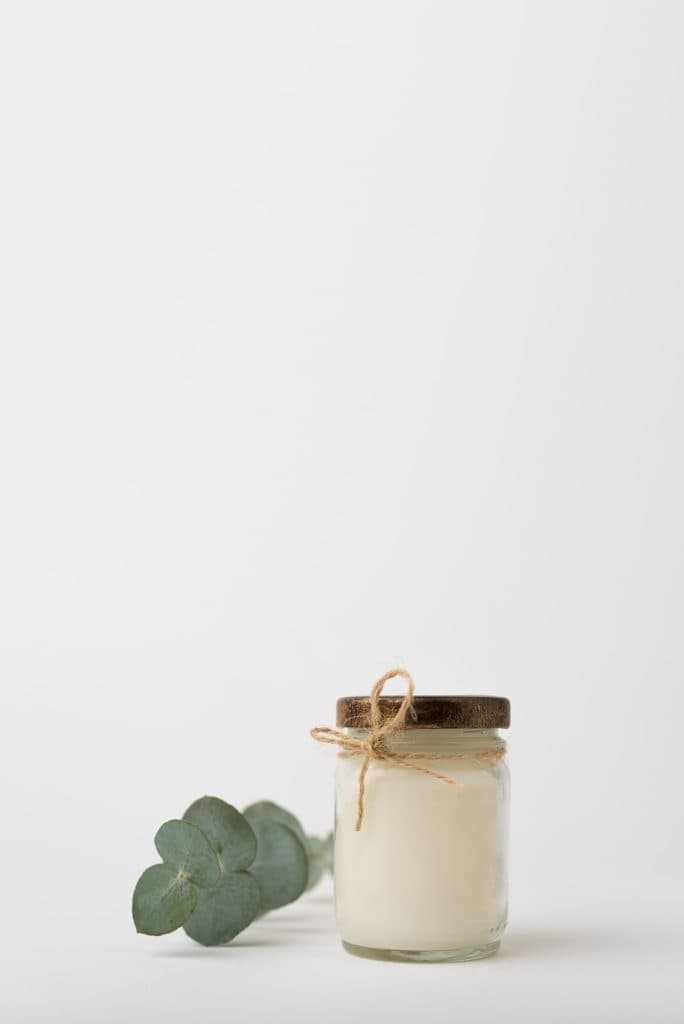 a beef tallow in a jar with a sprig next to it in a plain white background