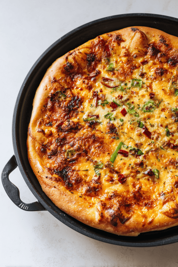 Freshly baked pizza on black round pizza pan, golden crust and bubbling toppings