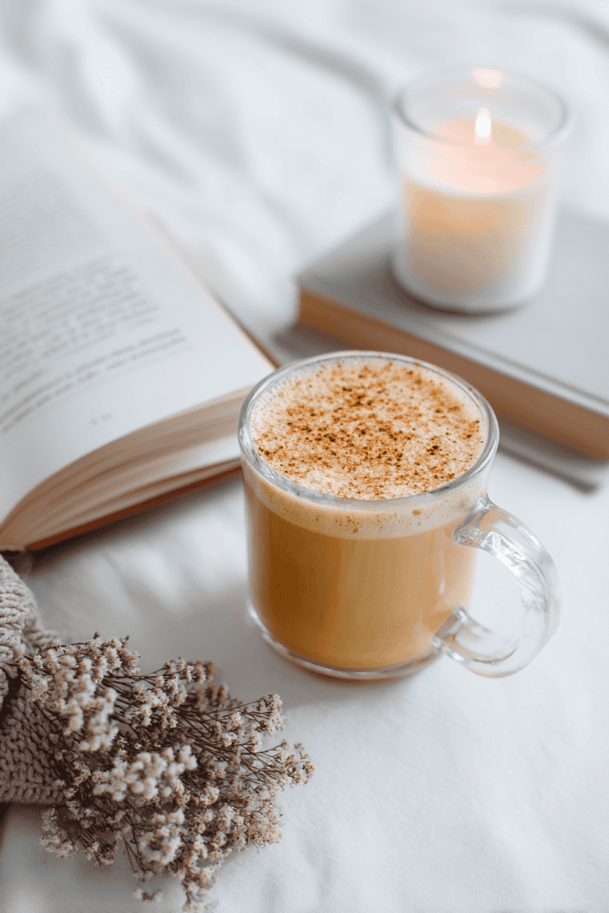 Healthy pumpkin spice latte in clear mug beside cozy candle and book