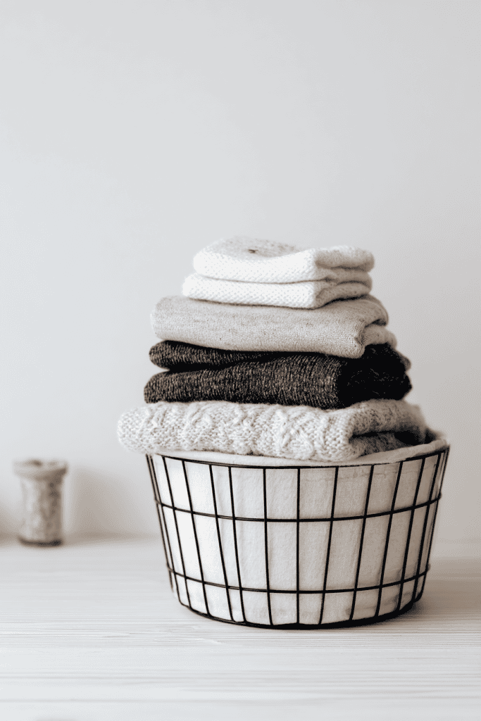 Minimalist toddler laundry setup, small neat stack of folded cotton and wool toddler clothes beside neutral laundry basket