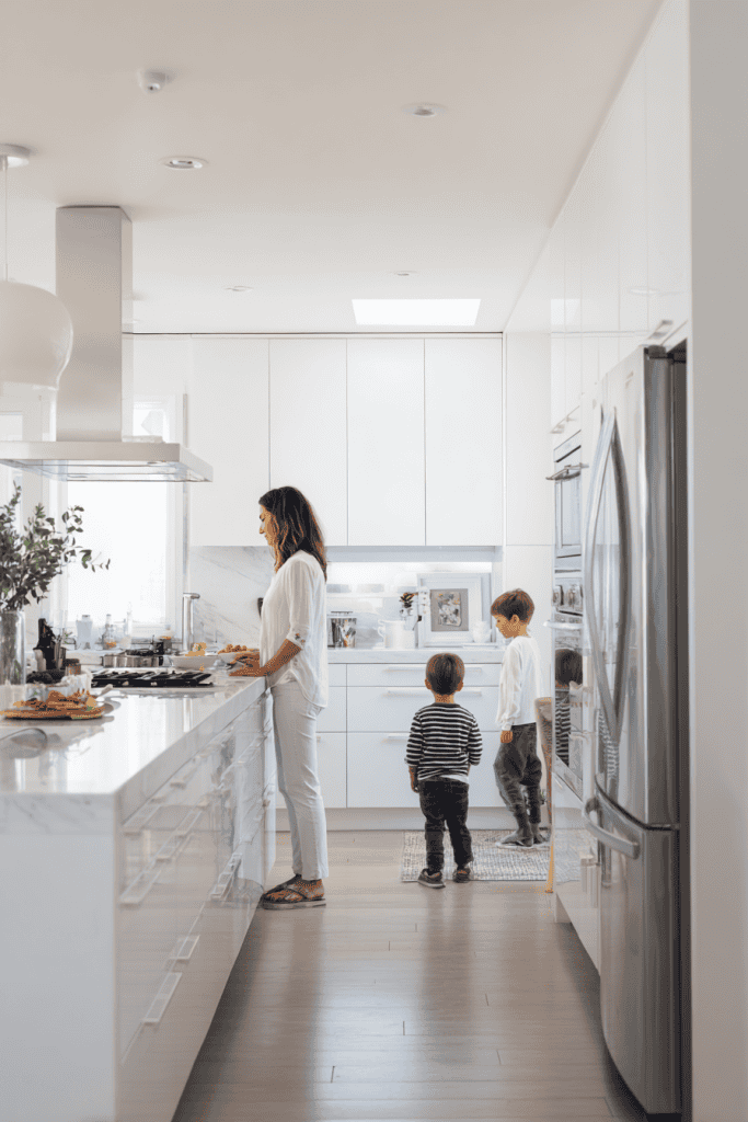 Mother in bright minimalist kitchen preparing breakfast while children enter