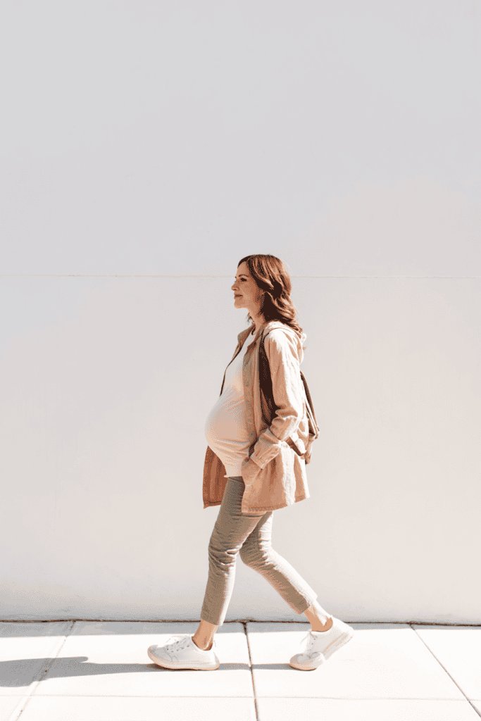 Pregnant woman walking to mailbox on bright path, relaxed posture