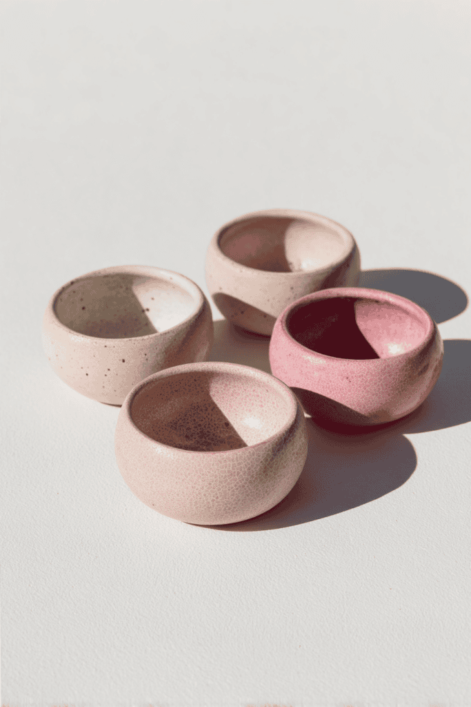 Small round clay tealight holders, shallow cup shapes with smooth rims, matte ivory and soft blush pink tones