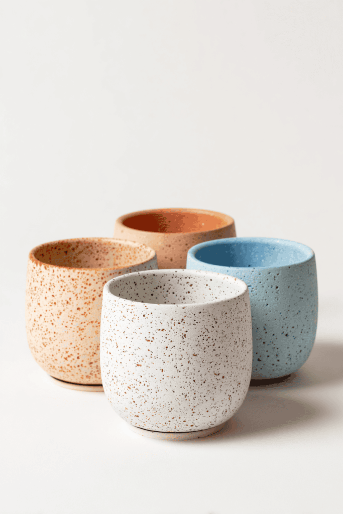 Collection of four small clay planters in assorted finishes: speckled white, soft blush pink, light terracotta, and pale sky blue