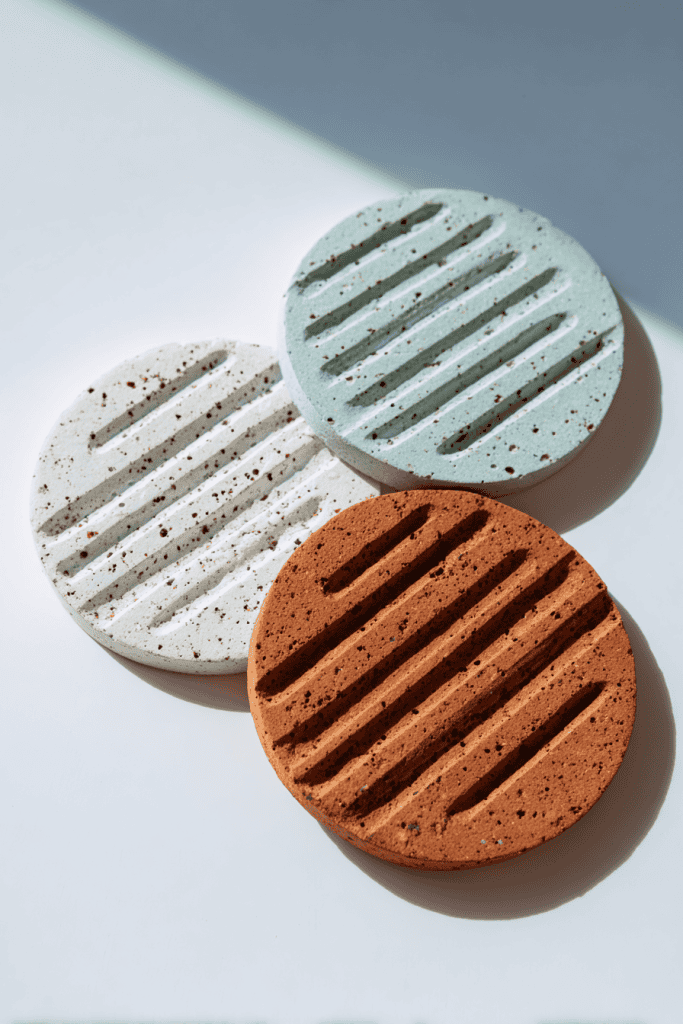Collection of three handmade clay trivets, one speckled white, one pale sky blue, one light terracotta with carved lines, arranged neatly side by side