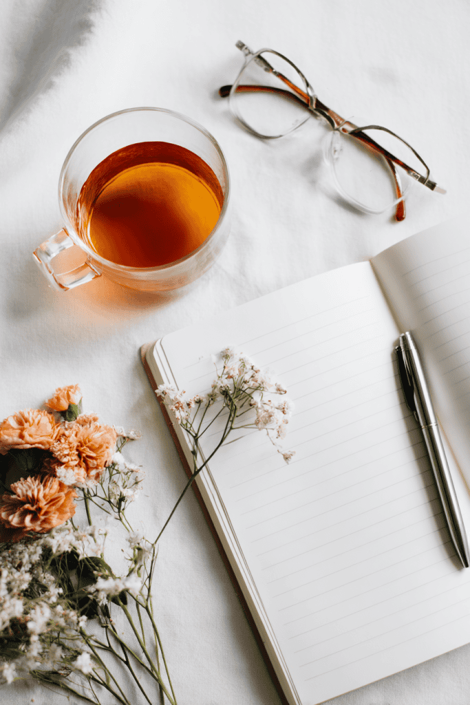 Flat lay of journal, pen, herbal tea, glasses