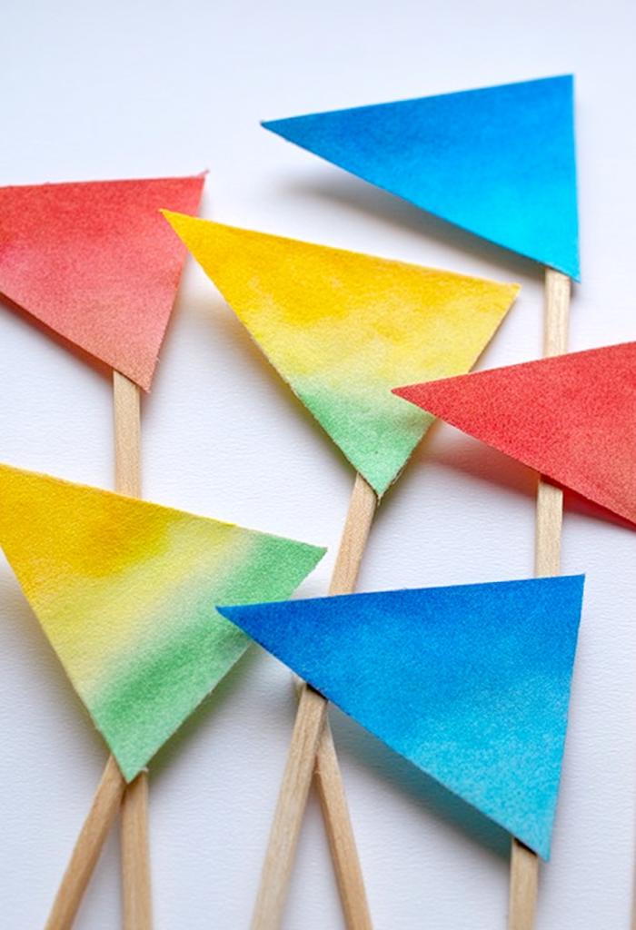 "Victory Banner Flags" inspired by the fall of Jericho. Handcrafted triangular flags made from colorful construction paper in bright, primary shades (red, blue, yellow, green), some with soft gradient blending