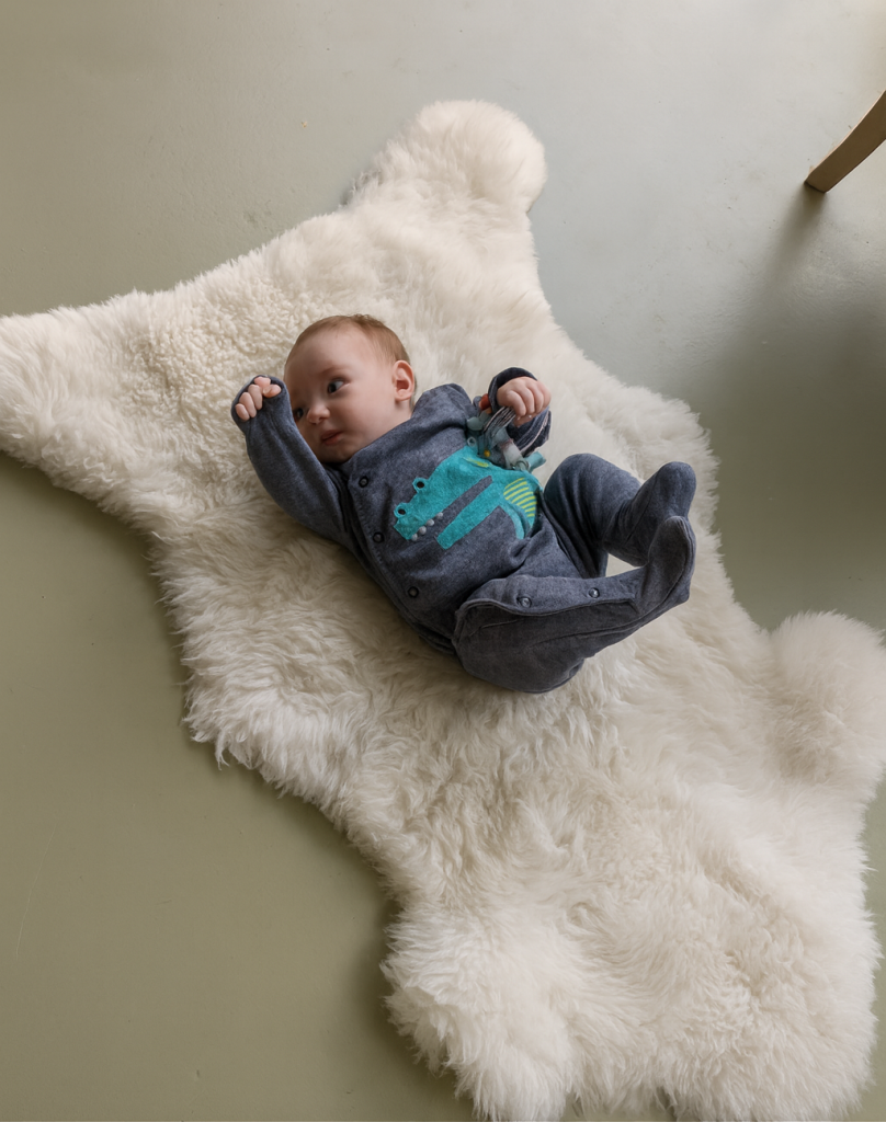  baby lying on a fluffy ivory-white sheepskin rug placed on a smooth, matte-finished concrete or light grey floor