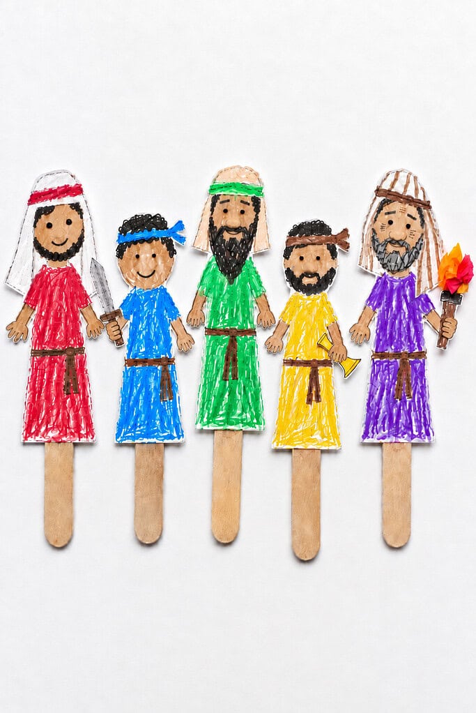 Five paper soldier stick puppets in red, blue, green, yellow, and purple crayon tunics glued onto wooden craft sticks, standing in a row, one holding a paper sword, one a trumpet, and one a tissue-paper torch.