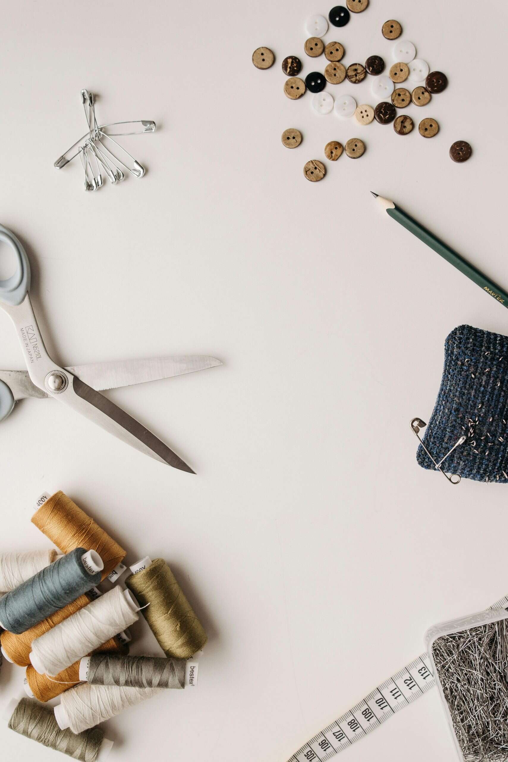 sewing tools on a table with thread spools, fabric scissors, buttons, safety pins, and measuring tape