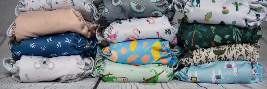 Multiple stacks of colorful cloth diapers arranged in rows on a white wooden surface