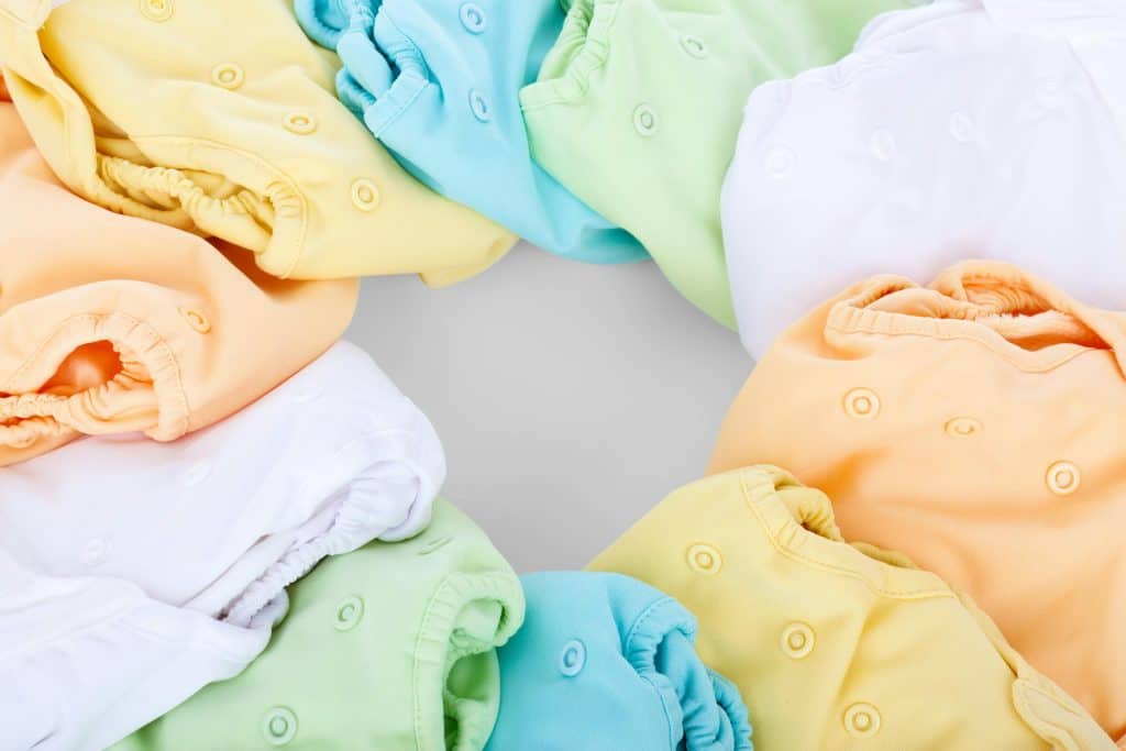 Pastel-colored cloth diapers arranged in a circular layout, featuring soft shades of yellow, mint green, baby blue, peach, and white.
