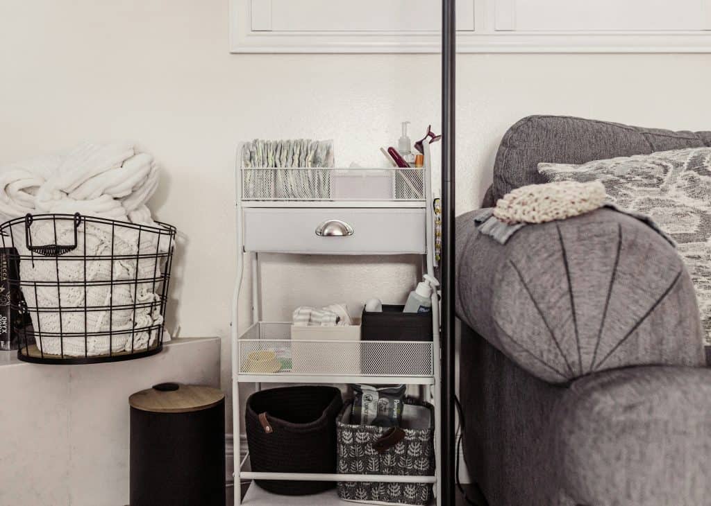 Cozy nursery corner with a white rolling cart stocked with diapers and baby essentials beside a gray upholstered chair