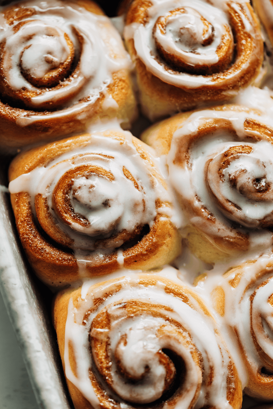 Freshly baked cinnamon rolls made with fresh milled flour, arranged neatly in a baking dish with light glaze drizzle, fluffy swirl texture visible