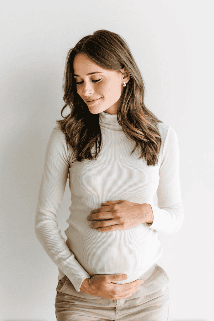 Pregnant woman in modern minimalist outfit, hands resting on belly, calm and confident expression