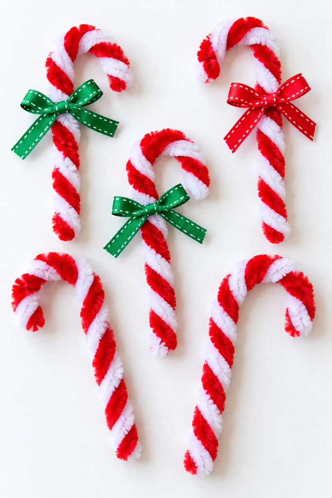 red and white twisted pipe cleaner candy canes with small ribbon bows laid side by side