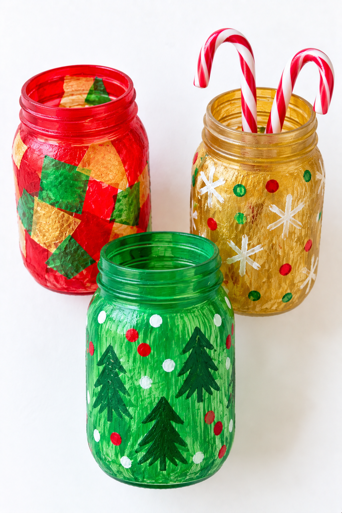 three mason jars painted in red, green, and gold with sponge patterns and tissue paper, one holding candy canes
