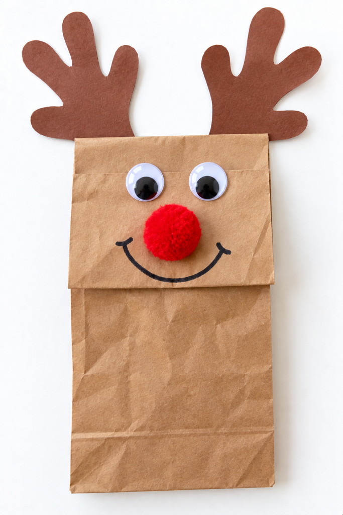 a paper bag reindeer puppet with construction paper antlers, googly eyes, a red pom-pom nose, and a drawn smile