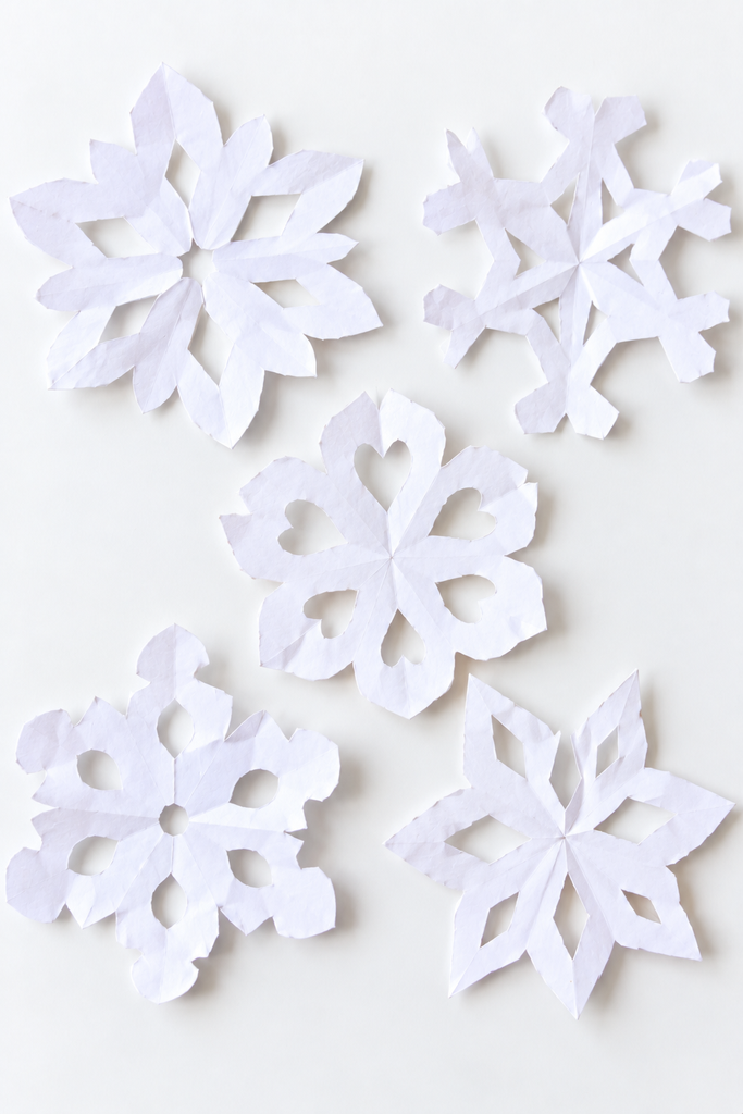 several hand-cut white paper snowflakes with lacy uneven patterns lying flat
