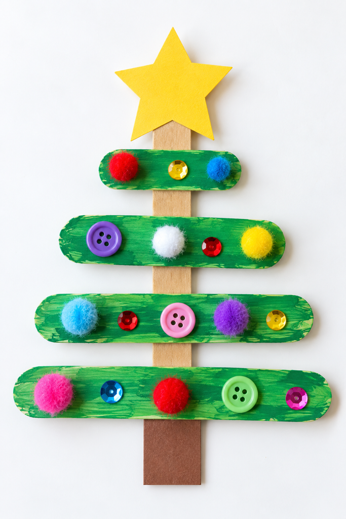 a popsicle stick Christmas tree craft painted green with pom-pom ornaments, a yellow paper star, and a brown paper trunk