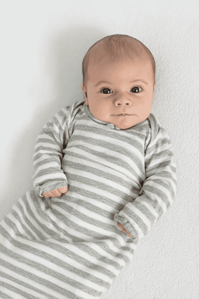 a newborn baby lying on their back on a soft, white surface, wearing a cozy, striped baby gown