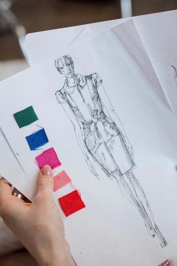 a fashion designer’s hand holding a sketch of a female garment design