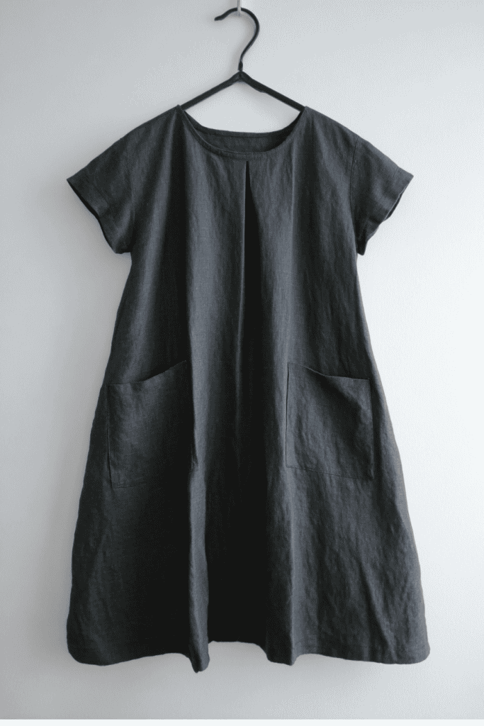 a minimalist dark gray linen dress hanging on a simple black hanger against a clean white wall