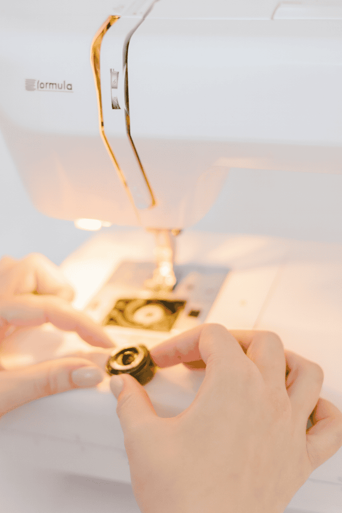 a person loading a bobbin into a modern white sewing machine