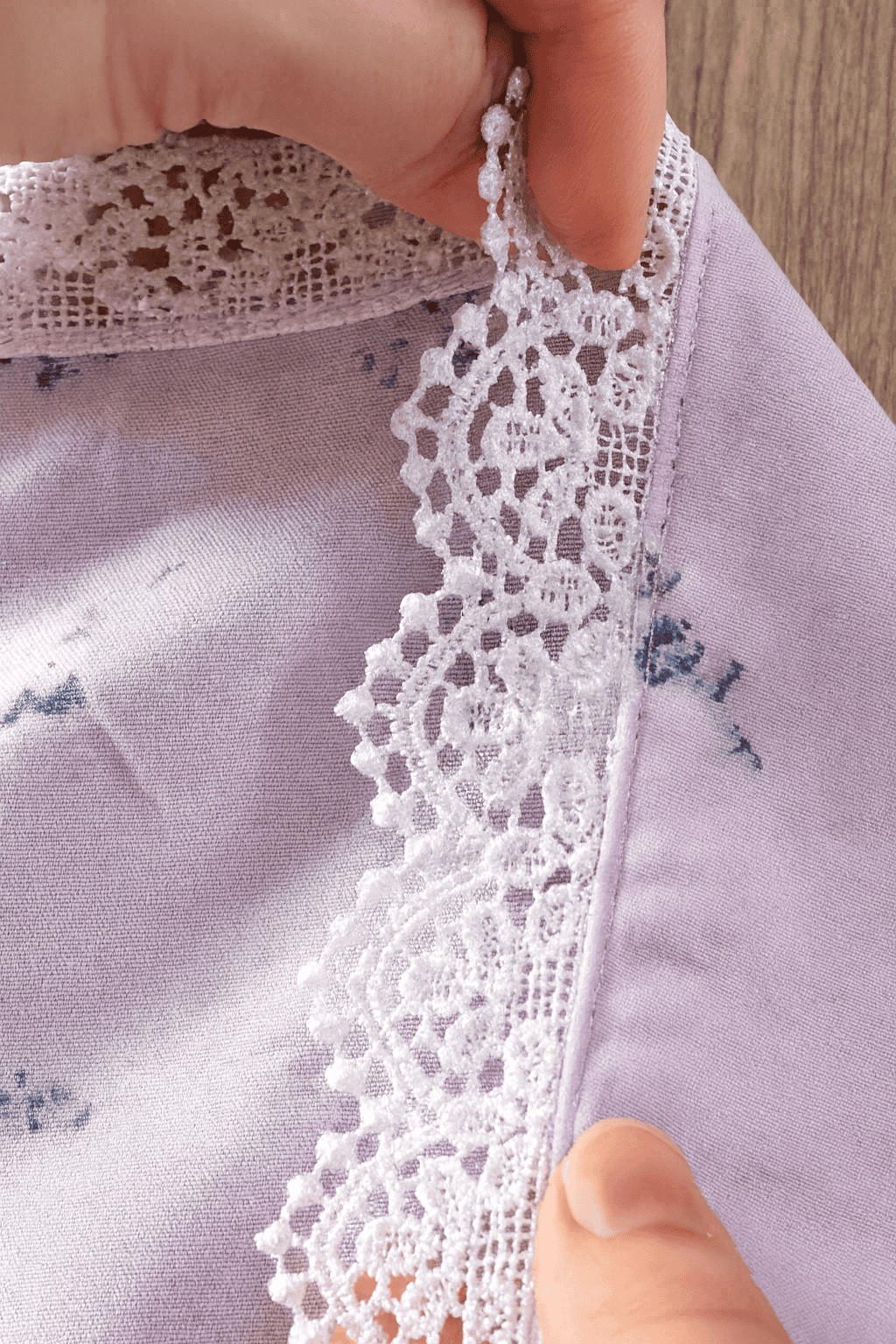 a piece of soft lavender fabric with delicate floral prints, showcasing a white lace trim sewn along the edge