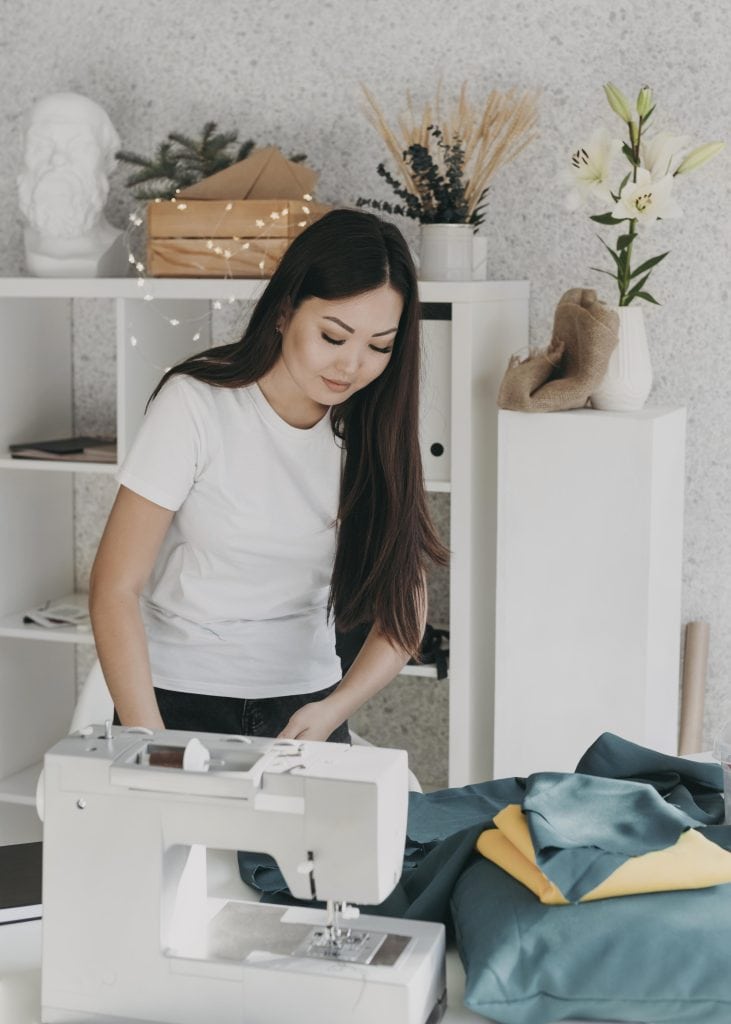 a young woman working with a white sewing machine in a stylish, cozy workspace.