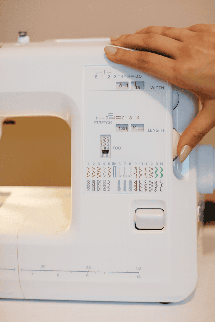 a modern white sewing machine with a person's hand adjusting the stitch width dial