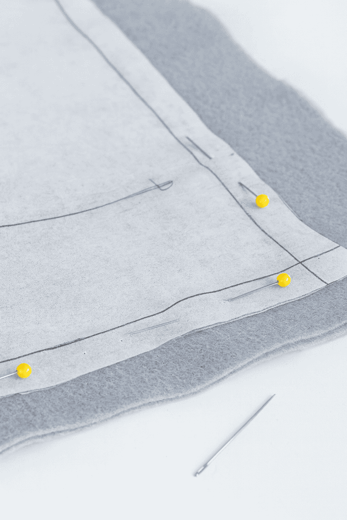 a piece of grey fleece fabric layered with white pattern paper, precisely pinned in place with yellow ball-head sewing pins
