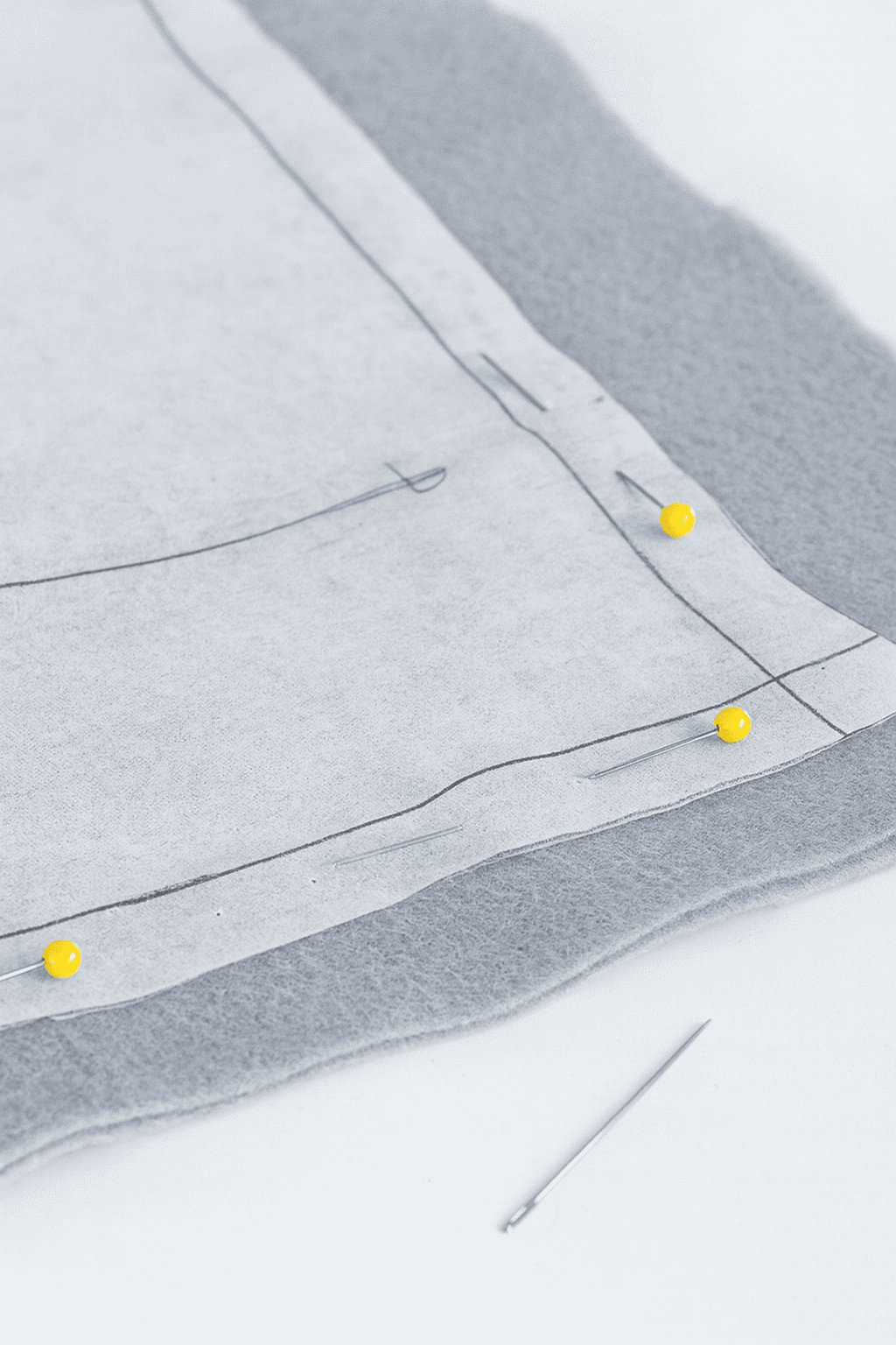 a piece of grey fleece fabric layered with white pattern paper, precisely pinned in place with yellow ball-head sewing pins