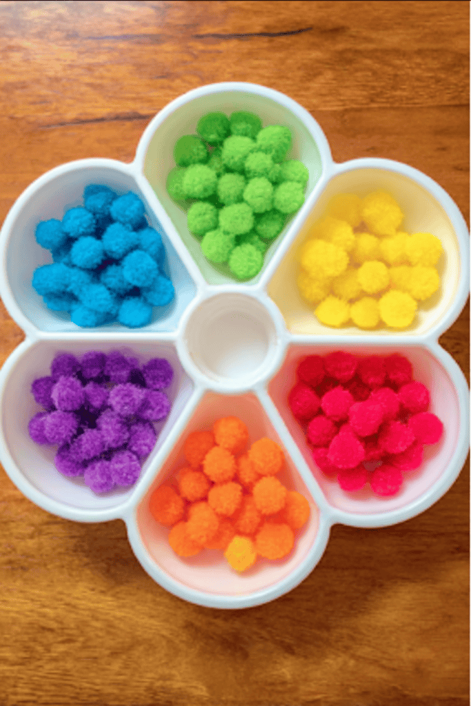 a white, flower-shaped sorting tray filled with small, colorful pom-poms used for sensory play and fine motor activities