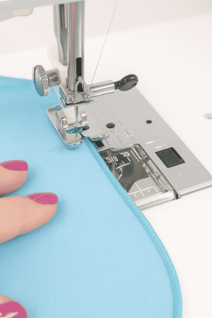 Close-up of a serger stitching a narrow rolled hem on light blue fabric, creating a smooth, neatly finished edge.