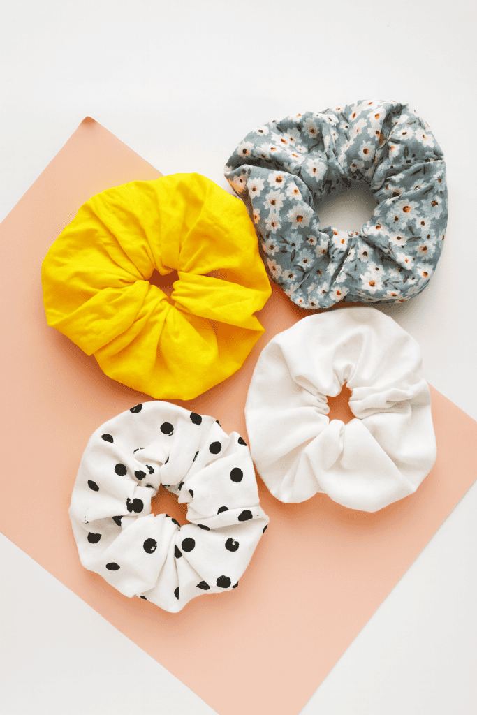 four handmade fabric scrunchies arranged on a soft peach and white background