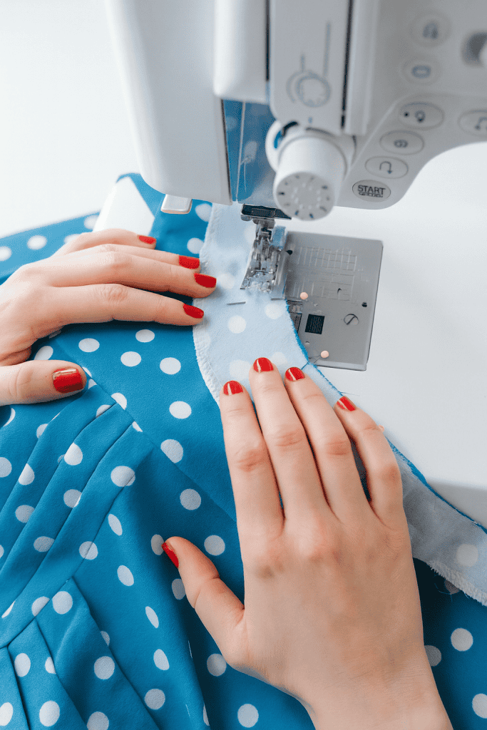 close-up of hands sewing blue polka dot fabric on a sewing machine, visible red nail polish