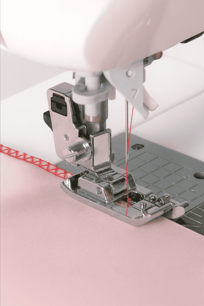 macro close-up of a sewing machine with overcasting presser foot stitching pink fabric using red thread