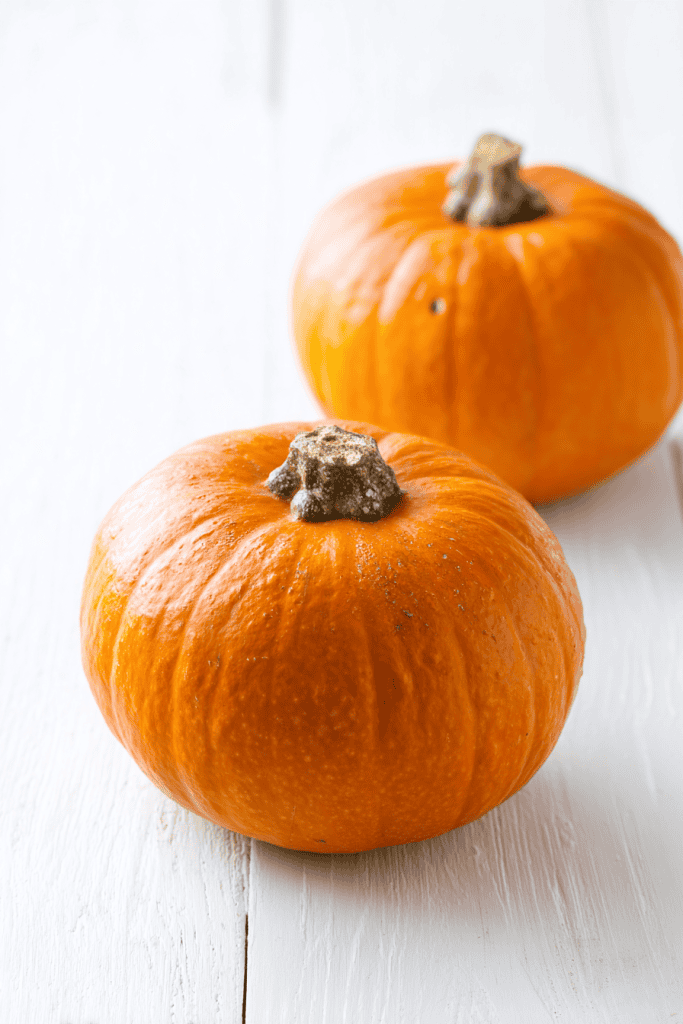 two whole sugar pumpkins placed on a clean white wooden surface
