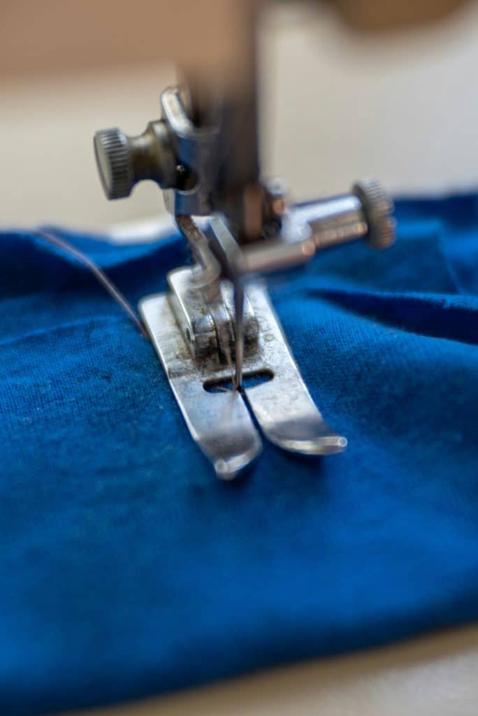 macro close-up of a sewing machine needle and presser foot stitching bright blue fabric