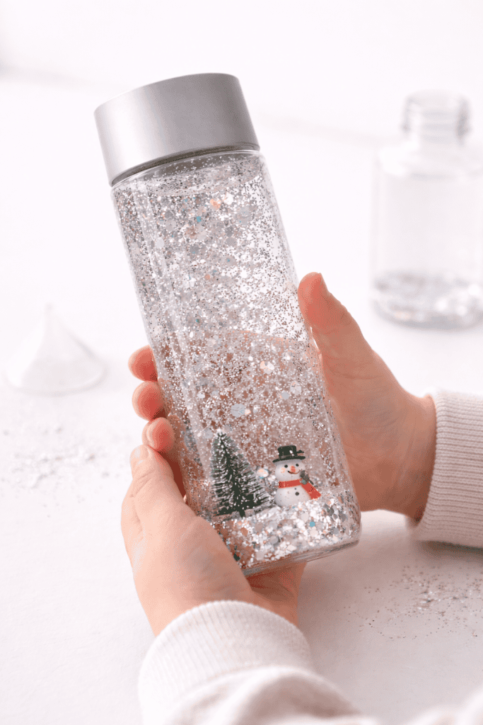 Toddler holding a clear sensory bottle filled with swirling silver glitter and small holiday figurines