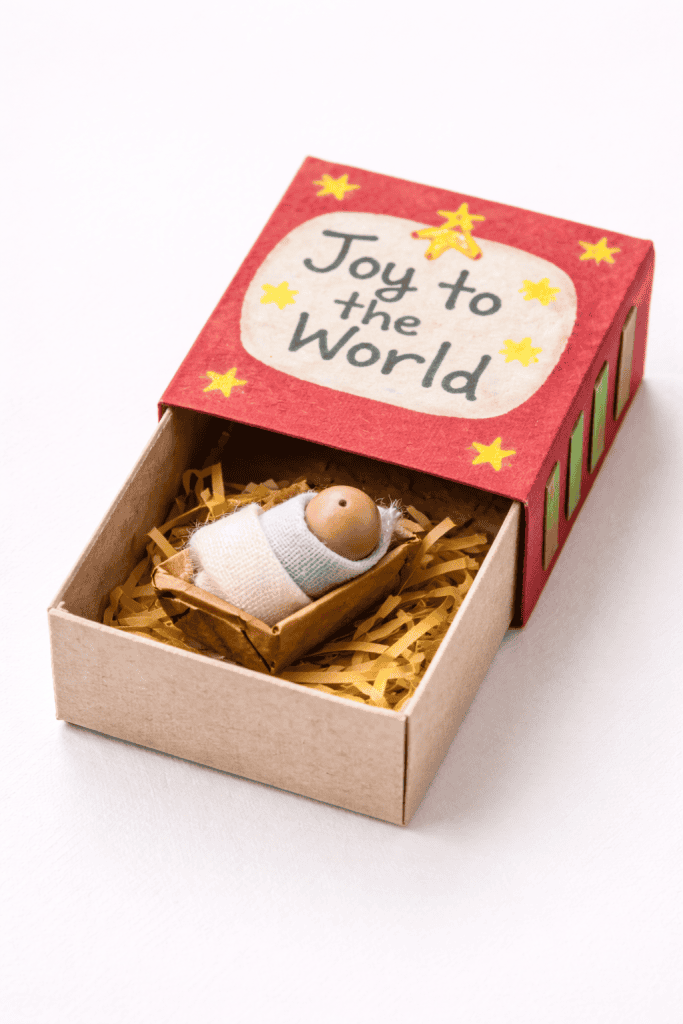 A small nativity-themed matchbox craft sits open on a white surface.