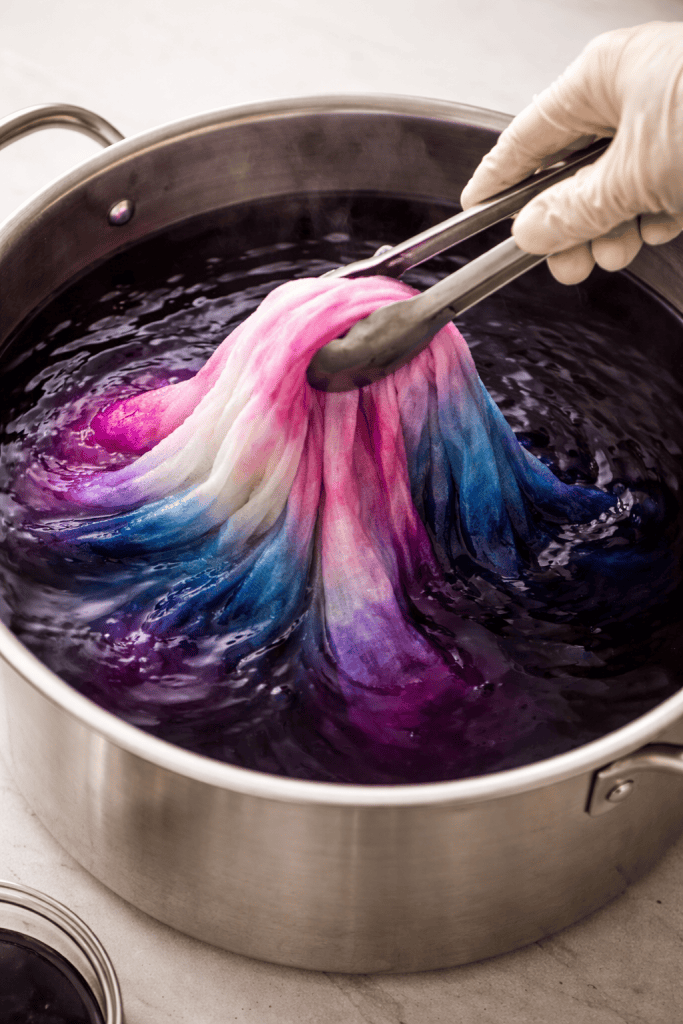 a damp cotton fabric being slowly submerged into a vibrant dye bath inside a large container.