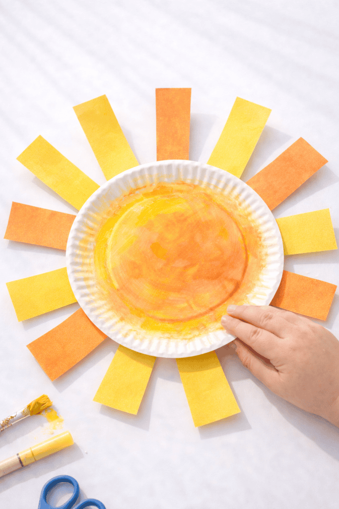 Paper plate sun craft for kids with yellow and orange rays, painted center, and simple supplies