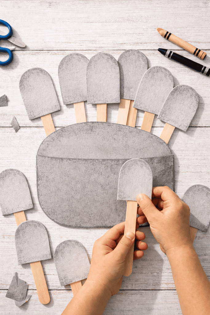 Ten small stone-shaped paper tablets, each mounted on a natural wooden popsicle stick to form handheld puppets.