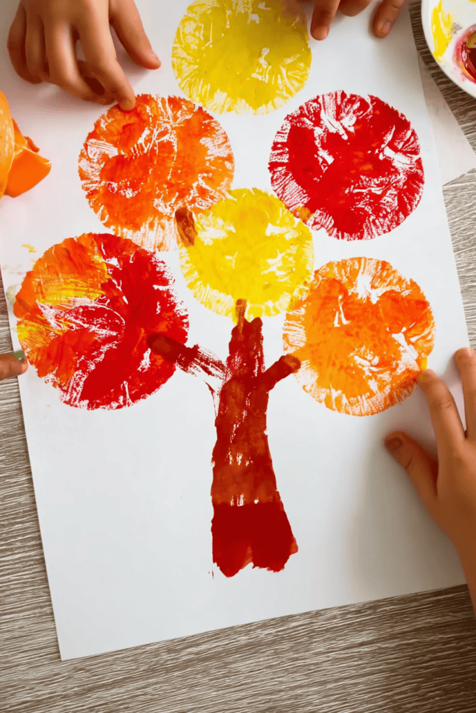 children’s hands creating apple print trees with red, yellow, and orange paint