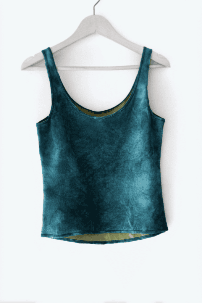 a hand-dyed, deep teal tank top hanging on a simple white hanger against a pure white background