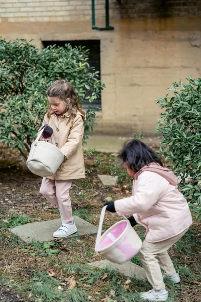 children in warm clothes with toy buckets playing in garden
