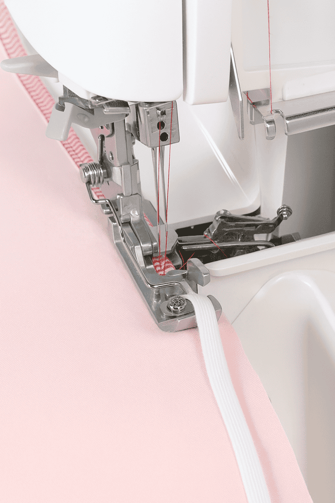 a serger (overlock) sewing machine stitching pink fabric while simultaneously attaching elastic using red thread